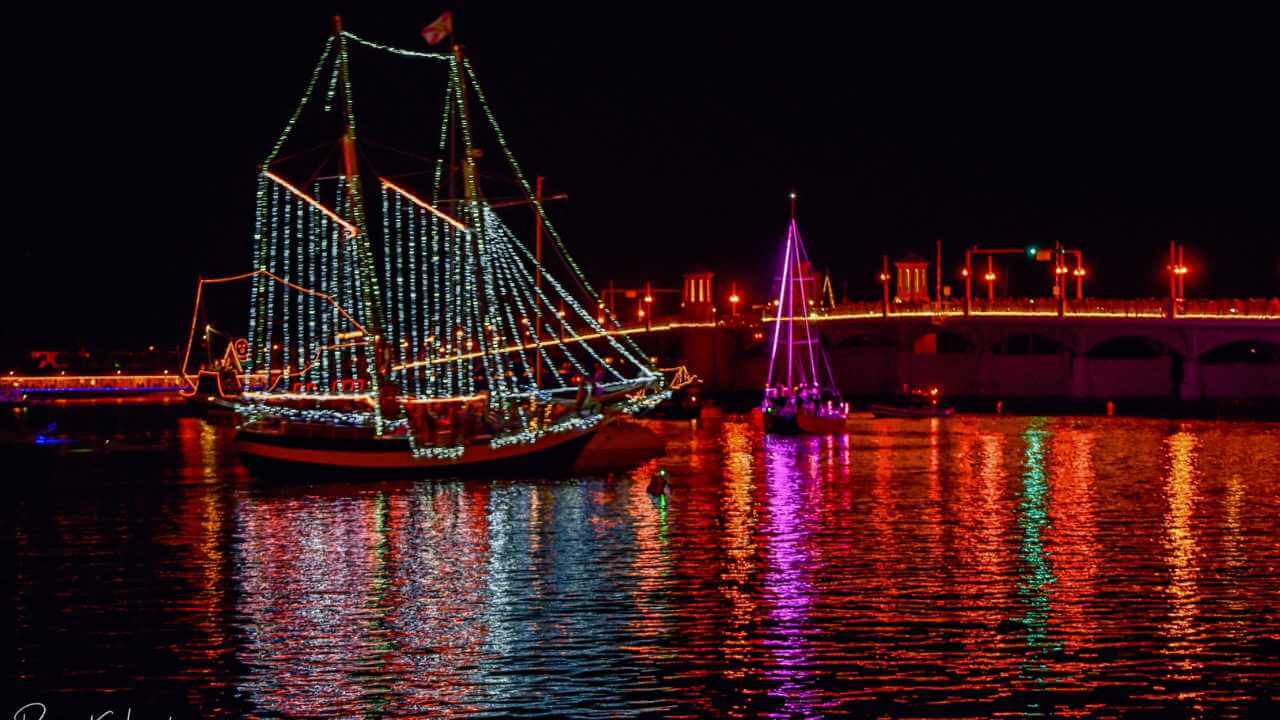 a sailboat in the water at night with a bridge in the background