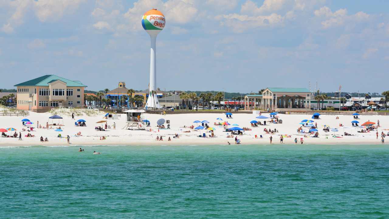 a beach with many people on it and a water tower in the background