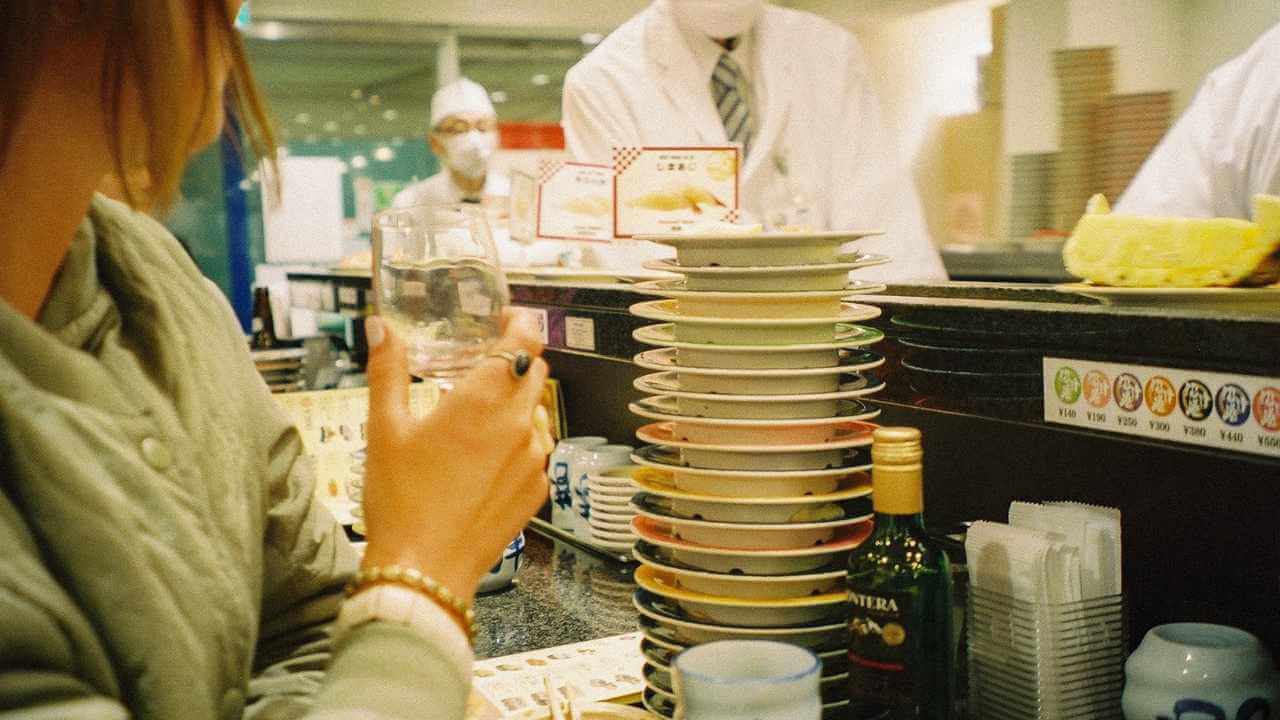 A person sitting at a sushi counter holding a glass of wine