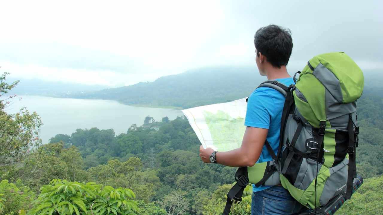 a person with a backpack looking at a map on top of a mountain