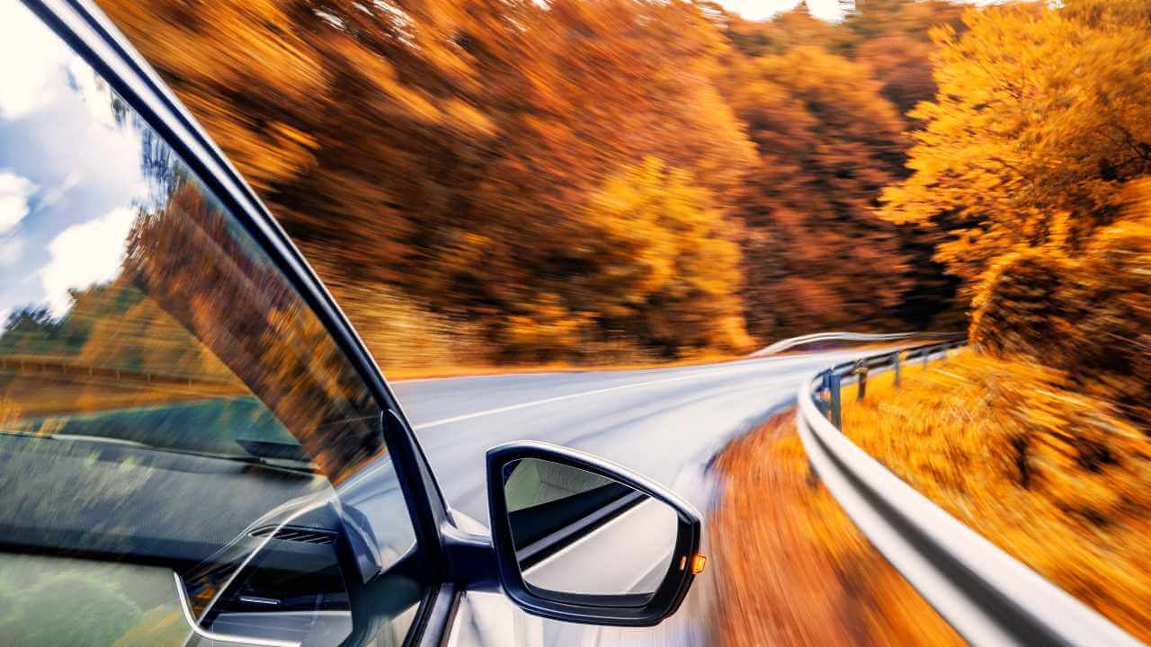 An automobile driving on the road with autumn trees in the background