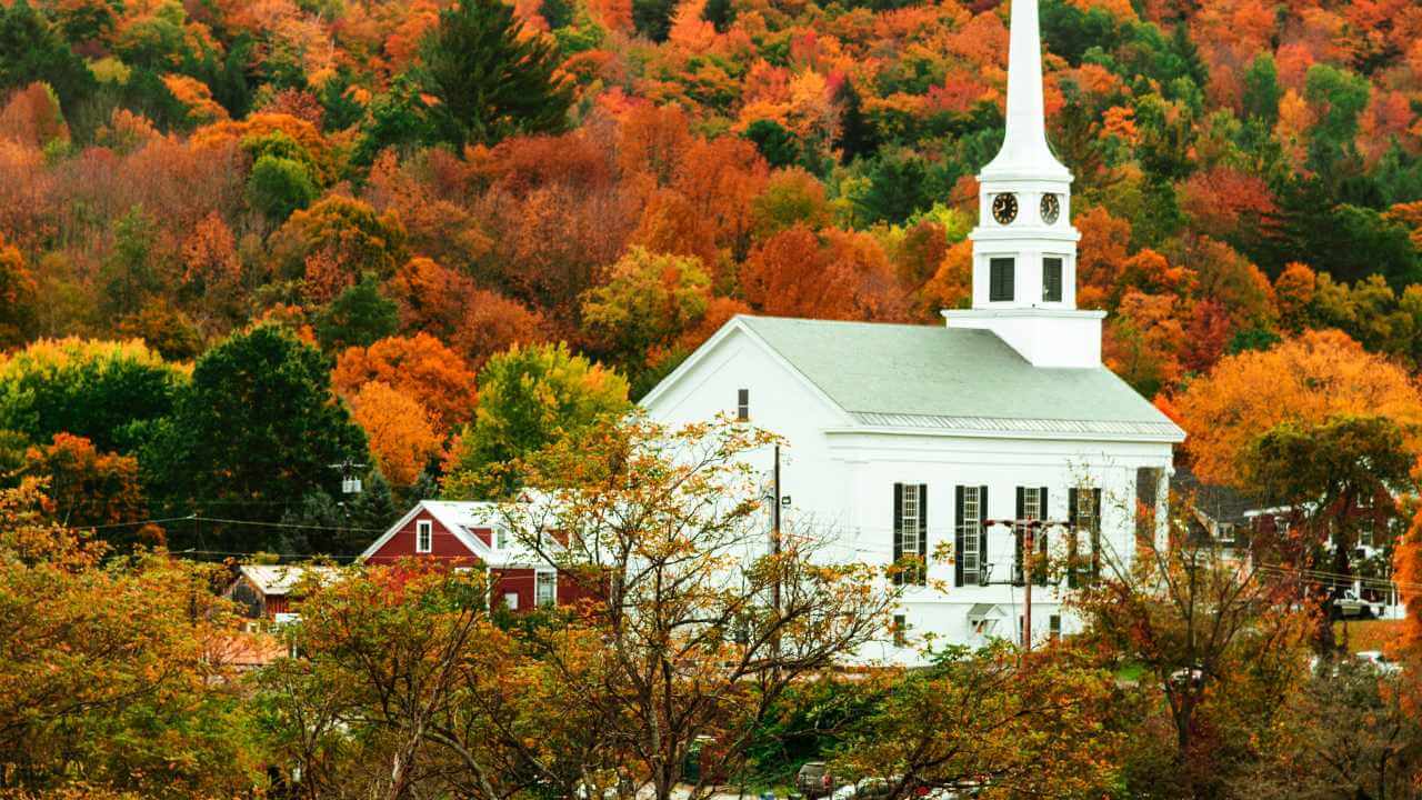 a church with a steeple on top of a hill surrounded by fall foliage