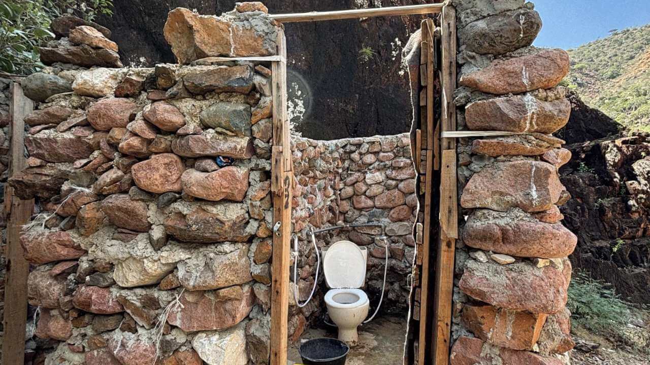 an outhouse with a toilet in the middle of a rock wall