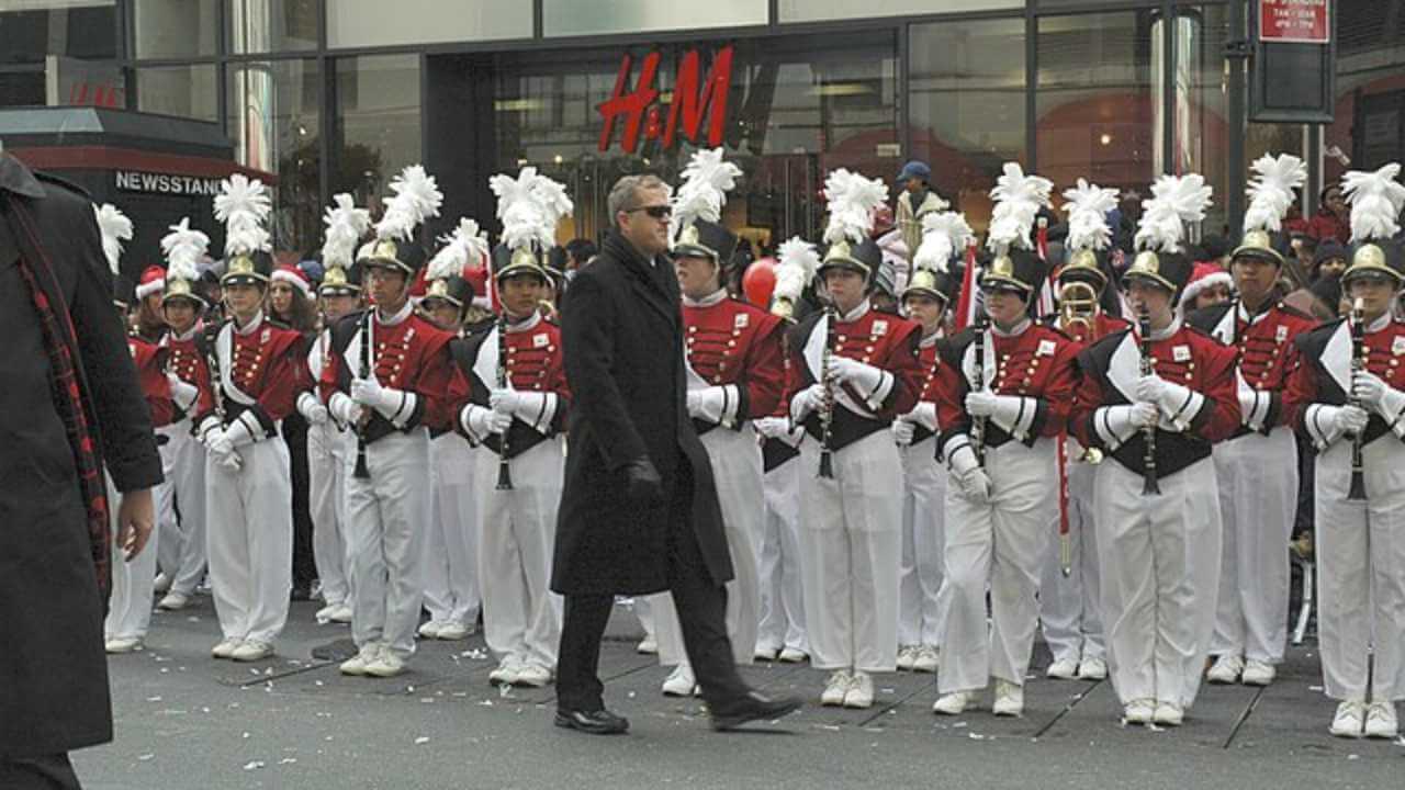 a person in a black coat walking in front of a marching band