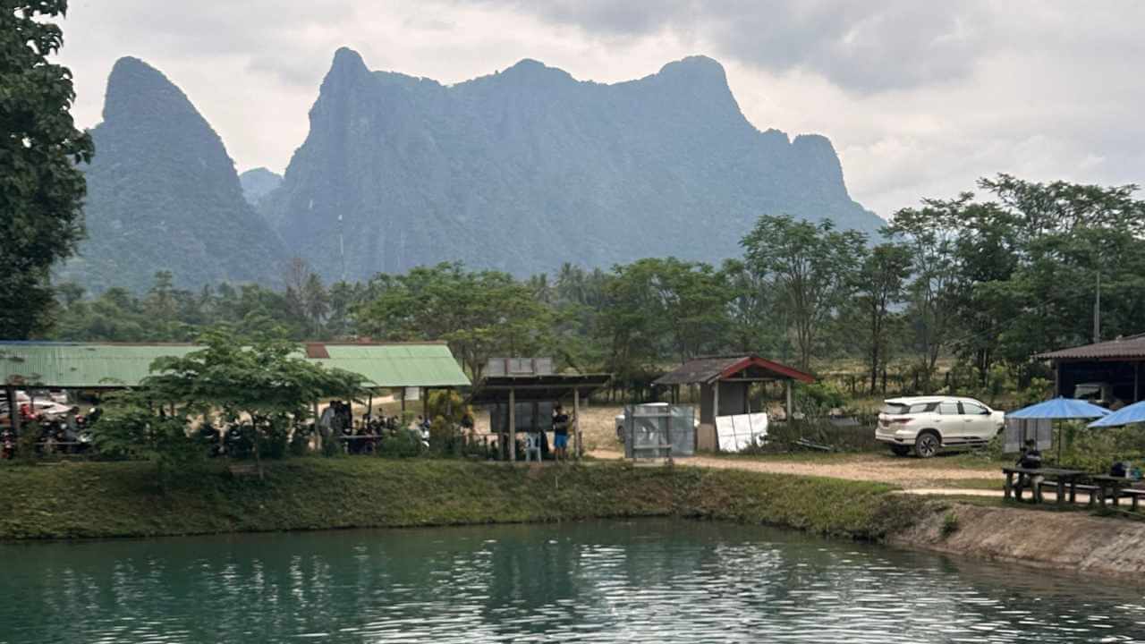 a group of people are sitting on the shore of a lake with mountains in the background