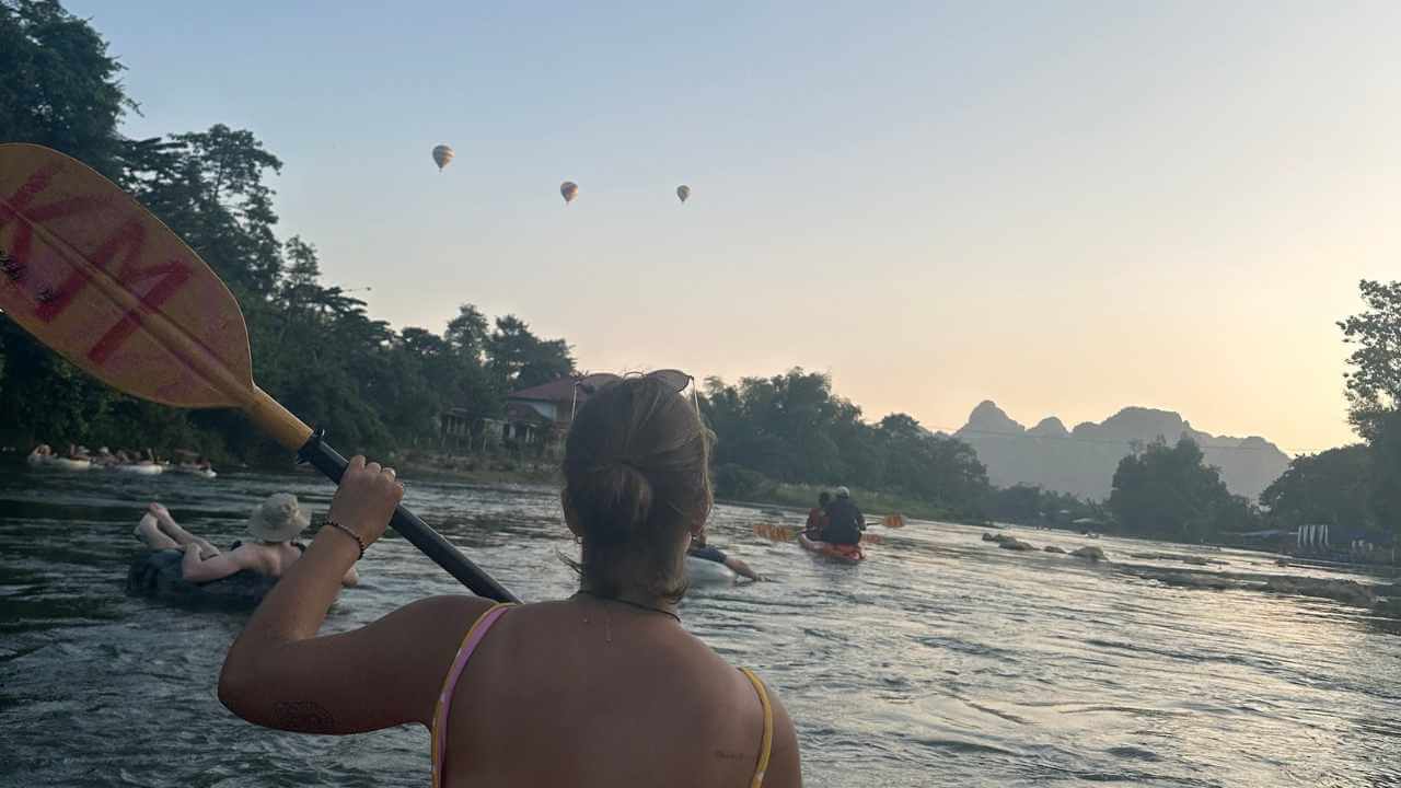 a person paddling a kayak down a river with hot air balloons in the background