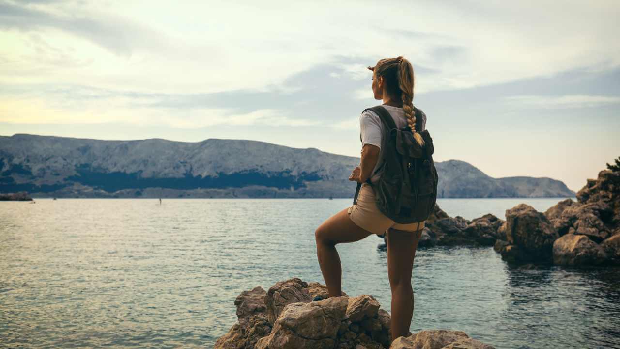 A person with a backpack standing on a rock overlooking the ocean