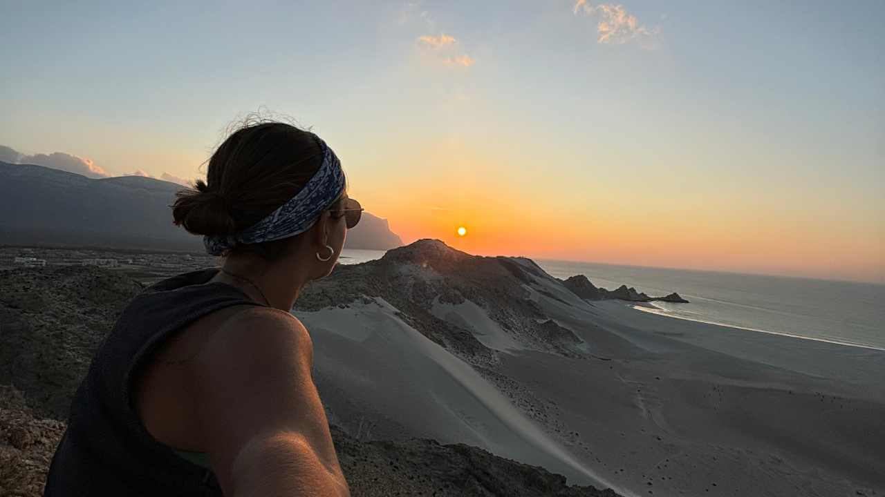 a person standing on top of a mountain overlooking the ocean at sunset