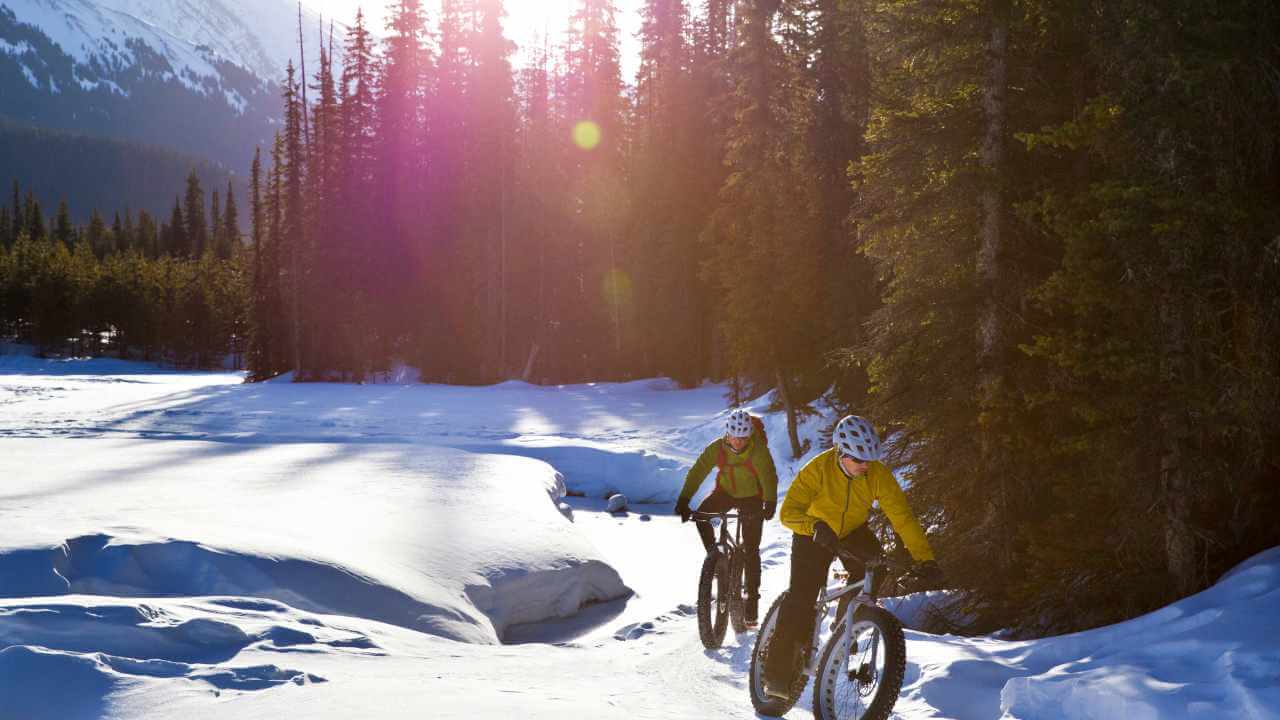 two people riding bikes on a snowy trail in the mountains