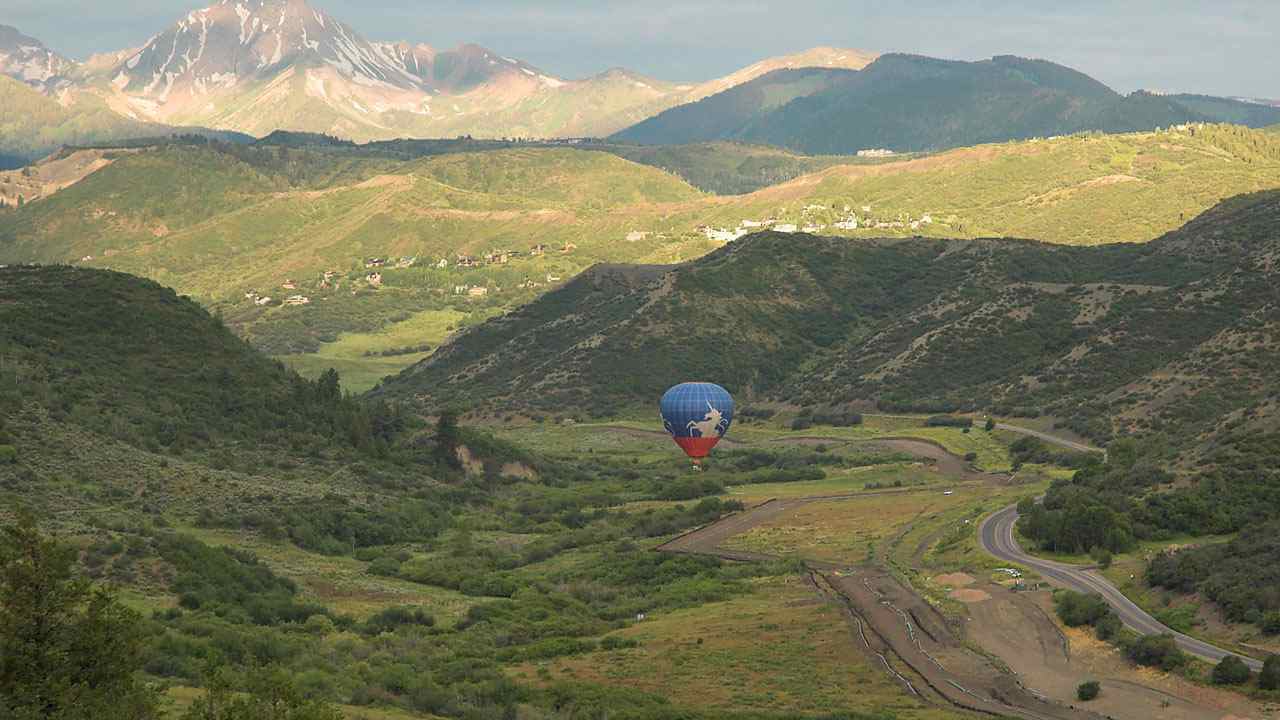 a hot air balloon is flying over a valley with mountains in the background