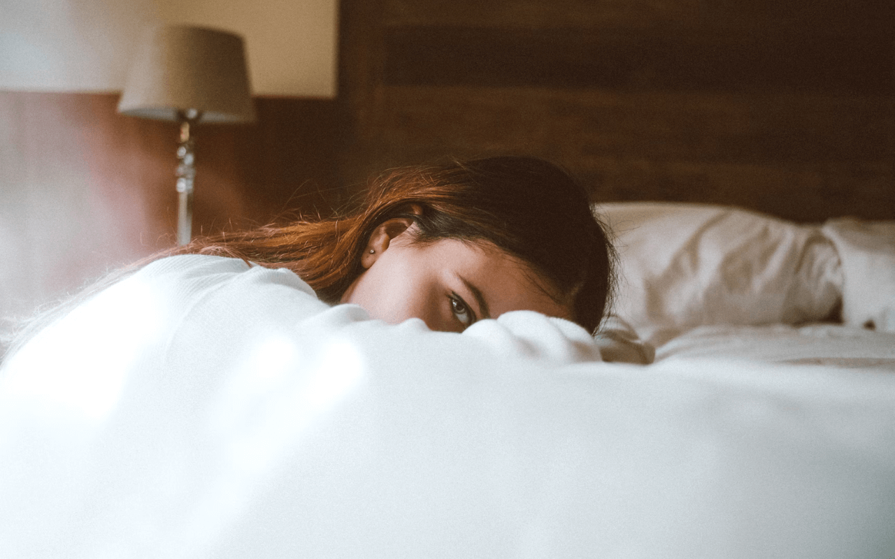 brown haired girl with one eye open laying on bed