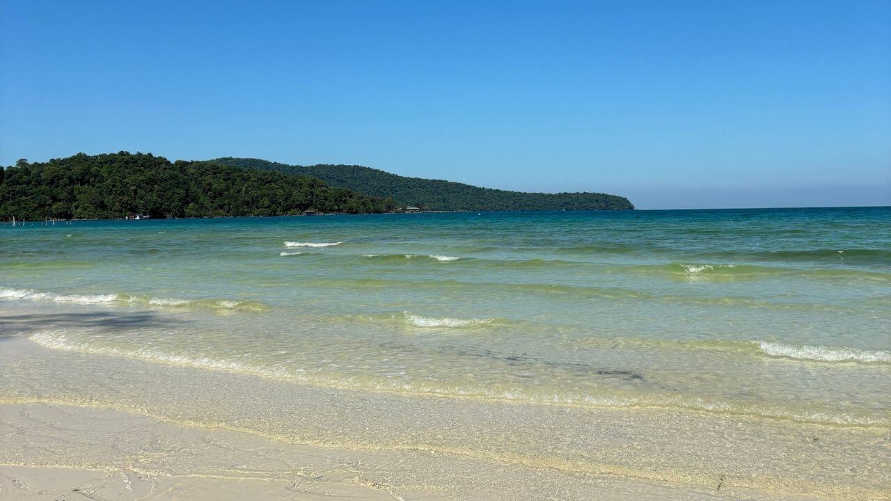 a white sandy beach with clear water and green trees