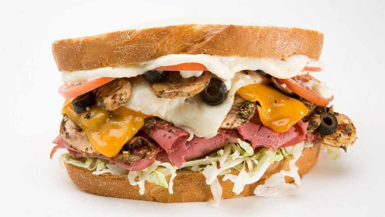 a sandwich with meat, cheese and vegetables on a white background