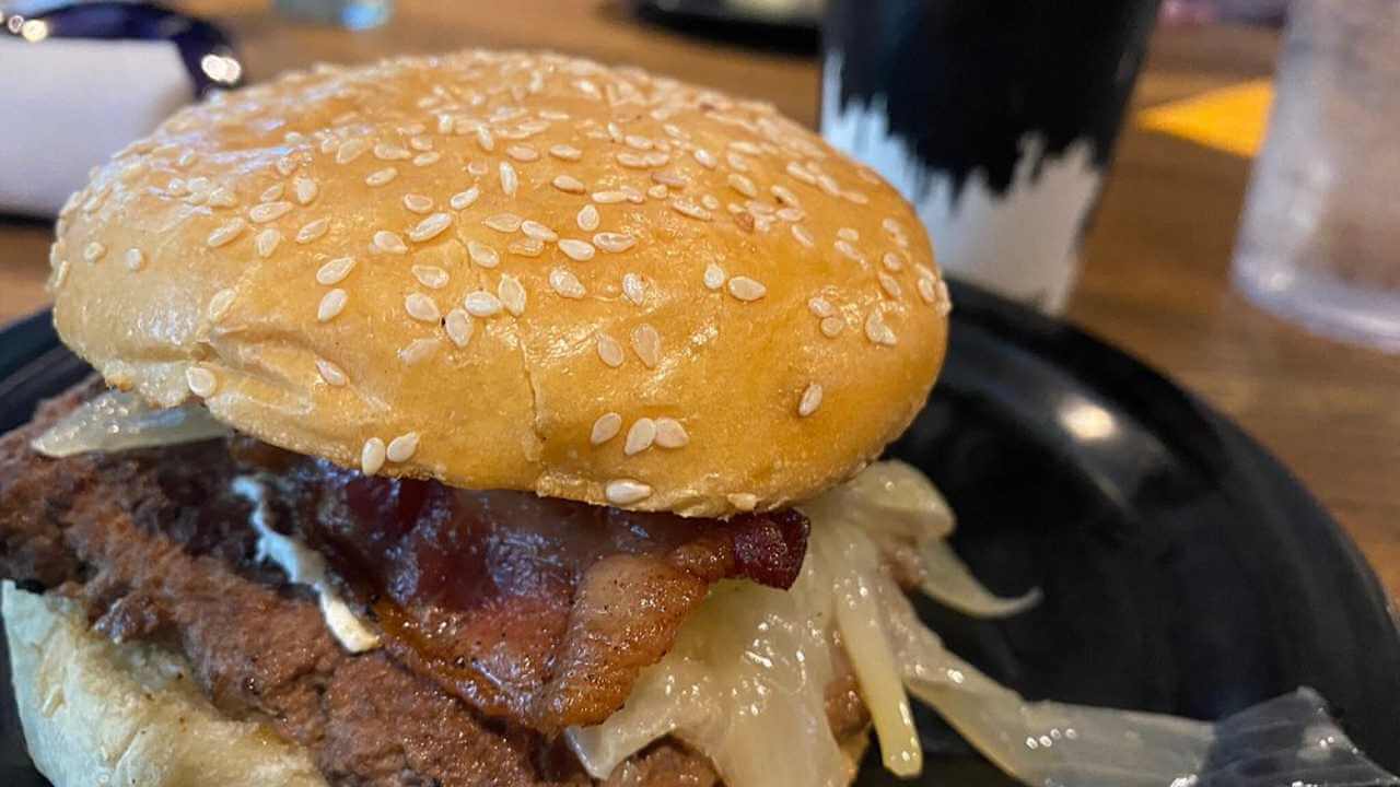 a hamburger with bacon and onions sitting on a black plate