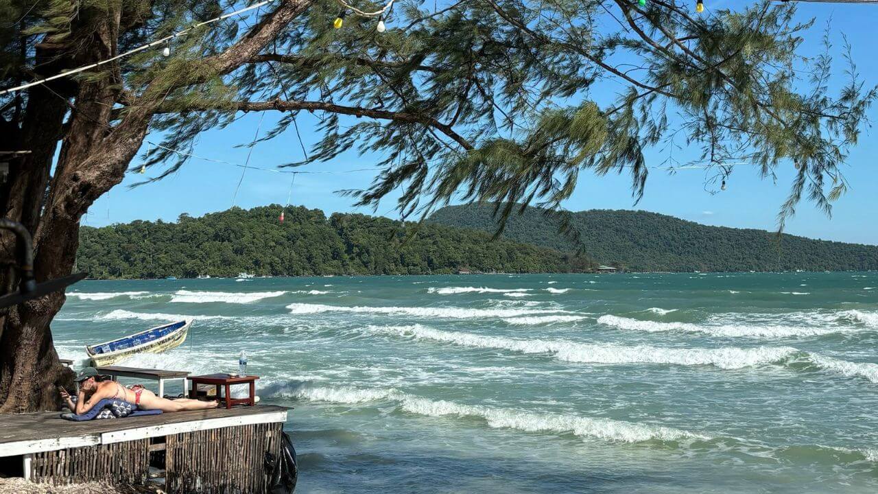 two people are relaxing on the beach next to a tree