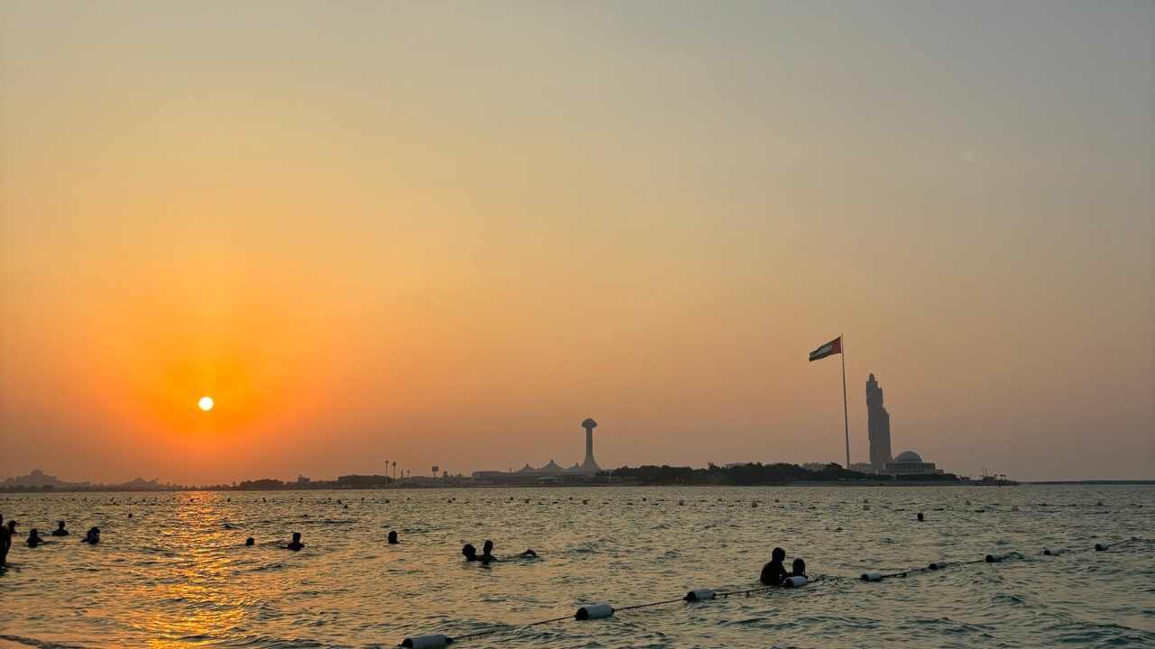 the sun is setting over a body of water with people swimming