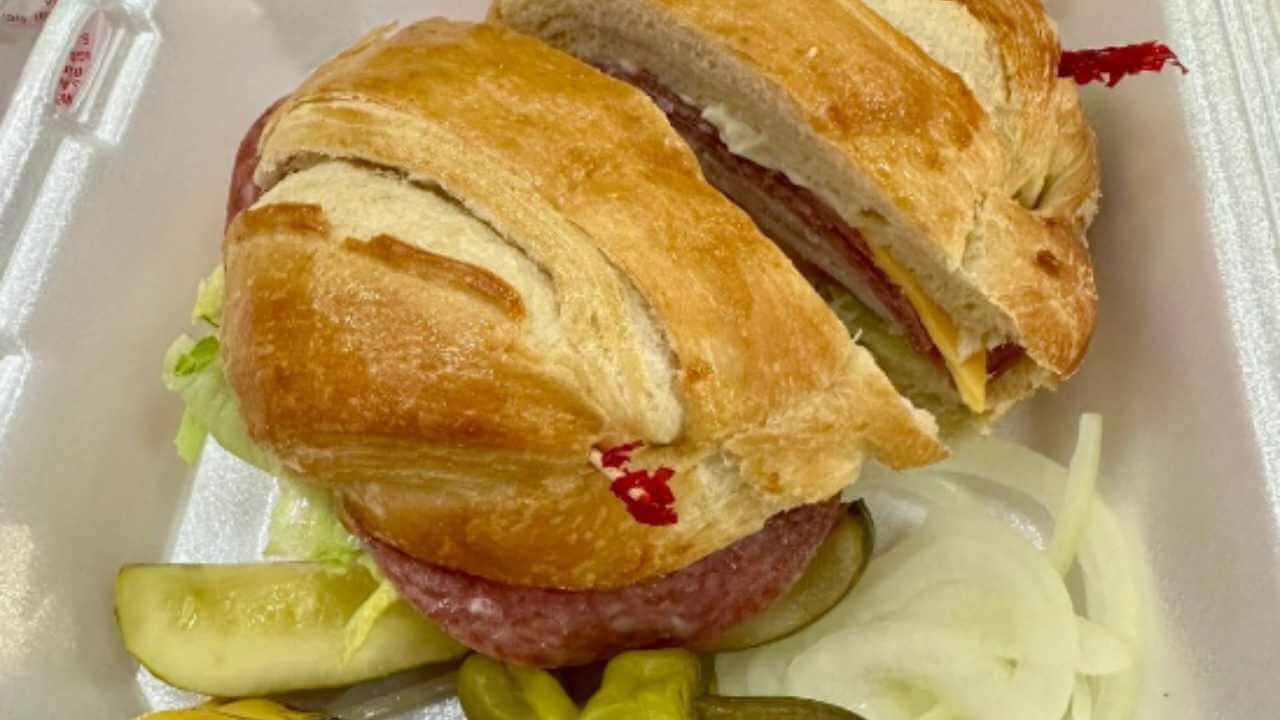 a croissant sandwich and pickles in a styrofoam container