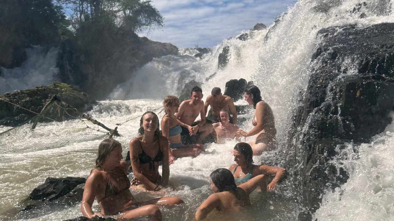 a group of people sitting in the water near a waterfall