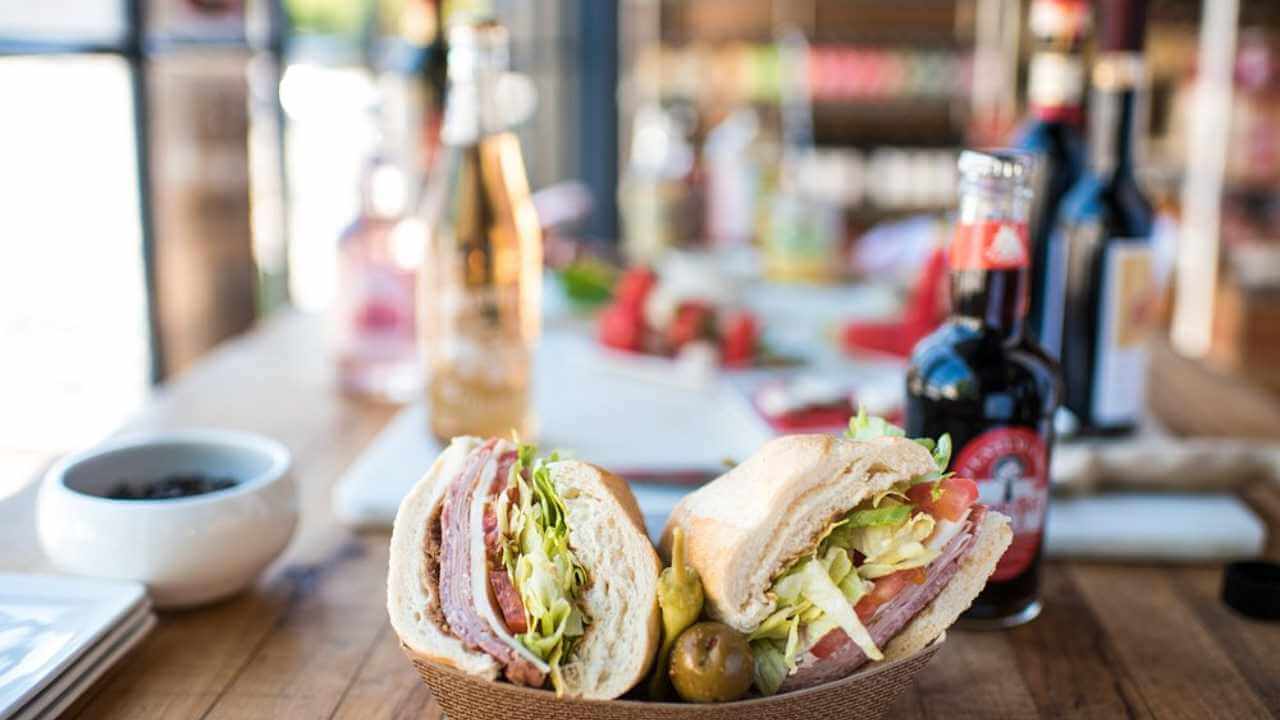 a sandwich sits on a wooden table next to a bottle of wine