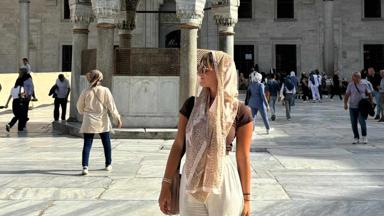a person wearing a headscarf stands in front of a fountain