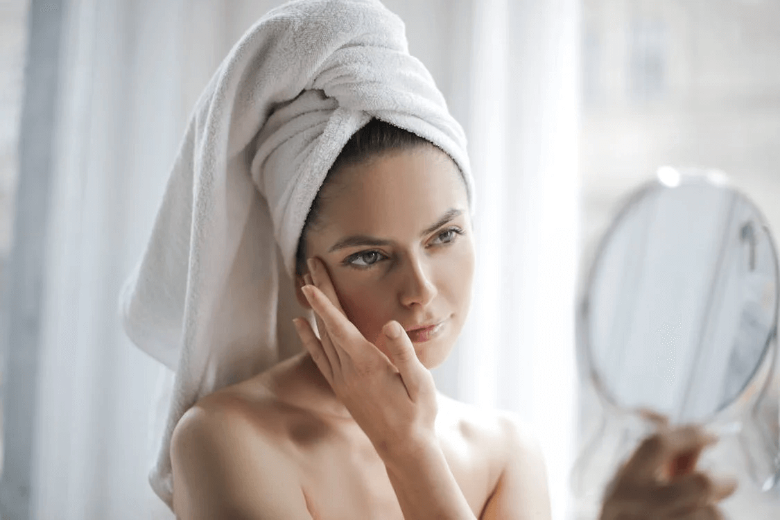 Woman with towel on her head looking in a mirror
