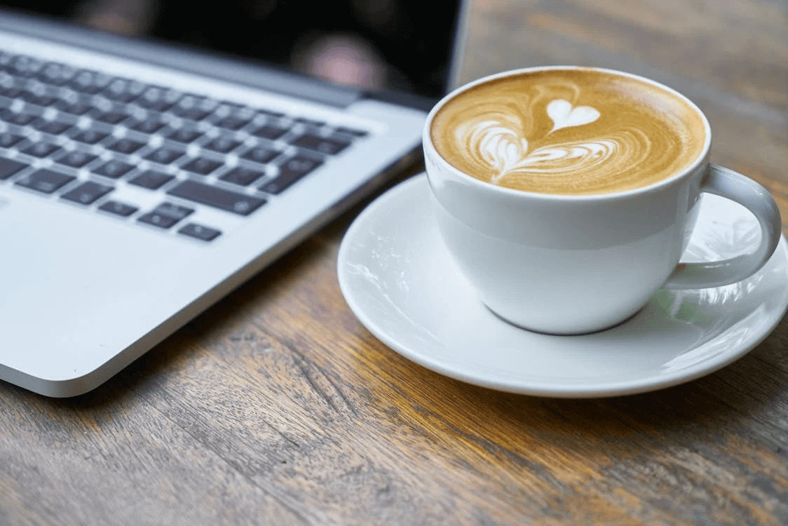 Cup of cappuccino next to a laptop