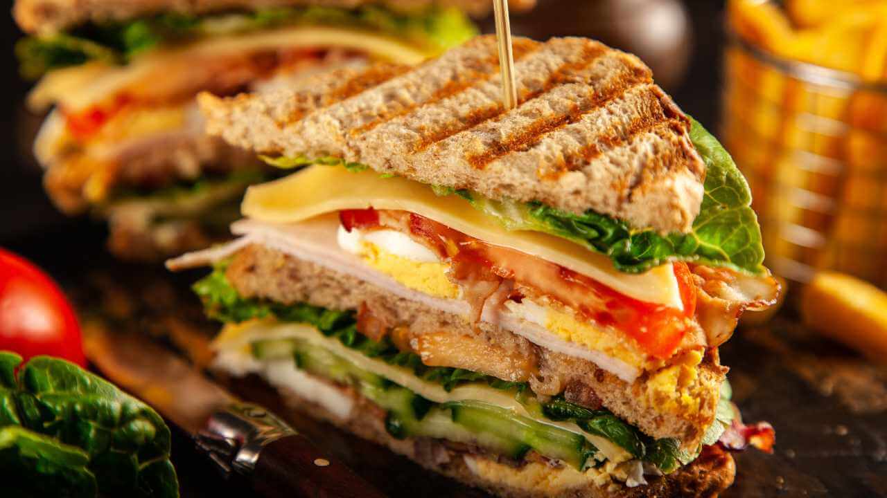 sandwich with chicken, lettuce, tomato and cheese on a wooden cutting board
