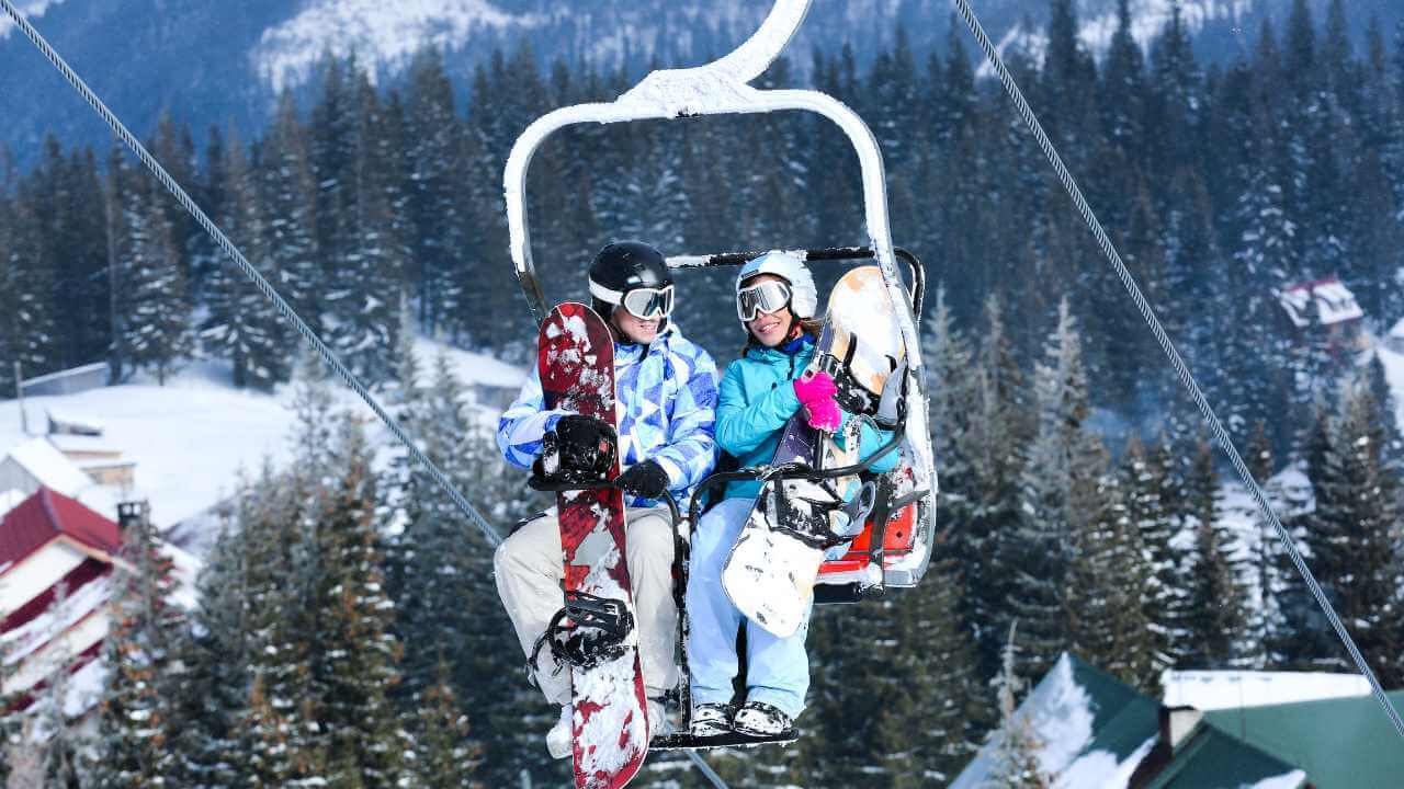 two people sitting on a ski lift with snowboards