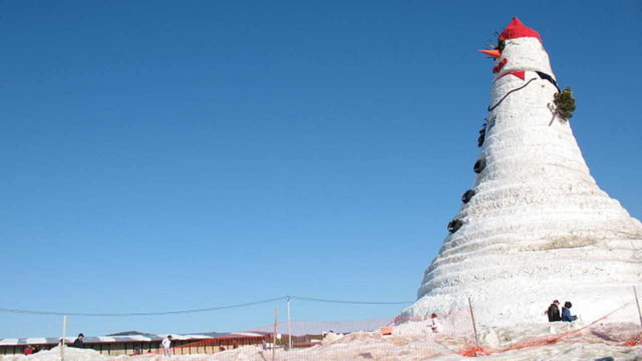a large snowman with a red hat on top of a hill