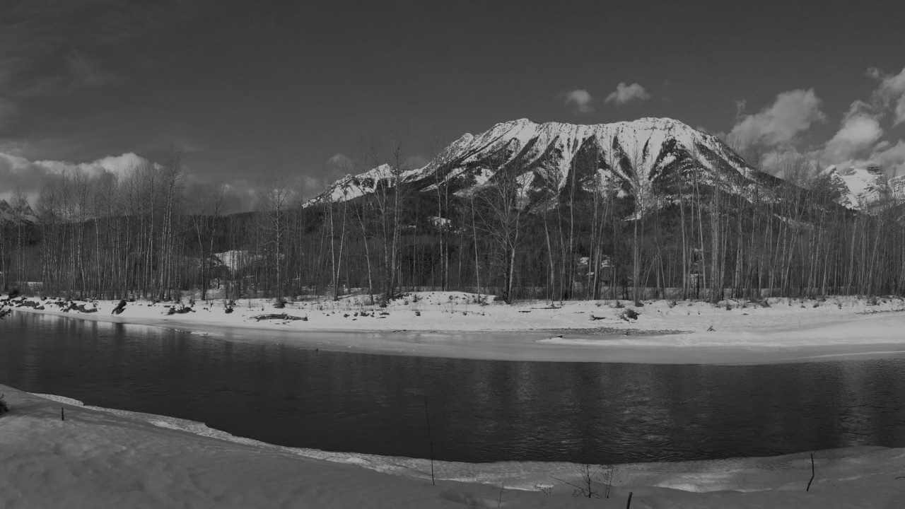 a black and white photo of a river and snow covered mountains