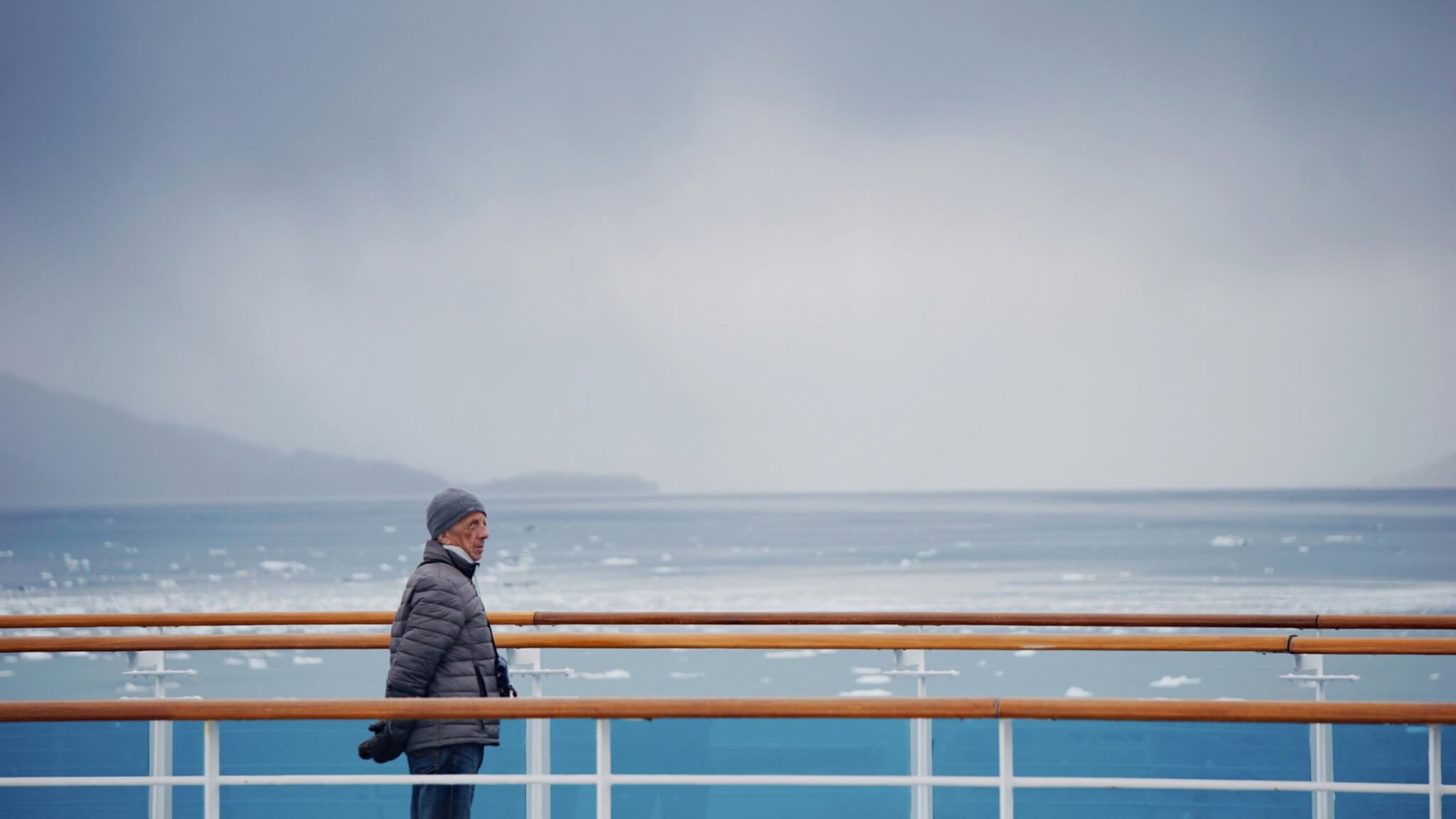 Person in warm clothing on Alaska cruise ship deck overlooking icy waters.