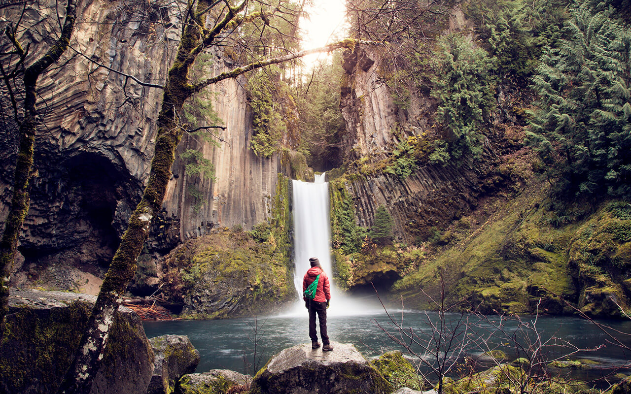 Traveler standing before a waterfall in lush forest, symbolizing underrated areas to buy a vacation home