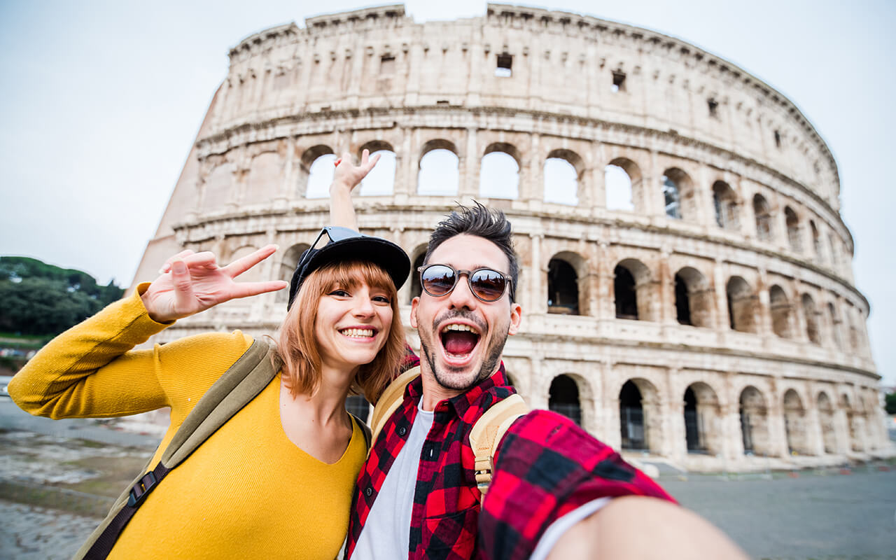 Happy couple of tourist smiling and taking a selfie at the Colosseum in Rome.