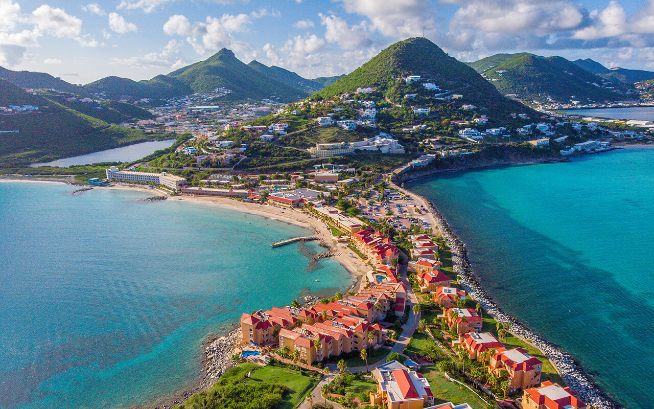 Aerial view of a Caribbean island with turquoise water, sandy shoreline, and colorful coastal buildings.