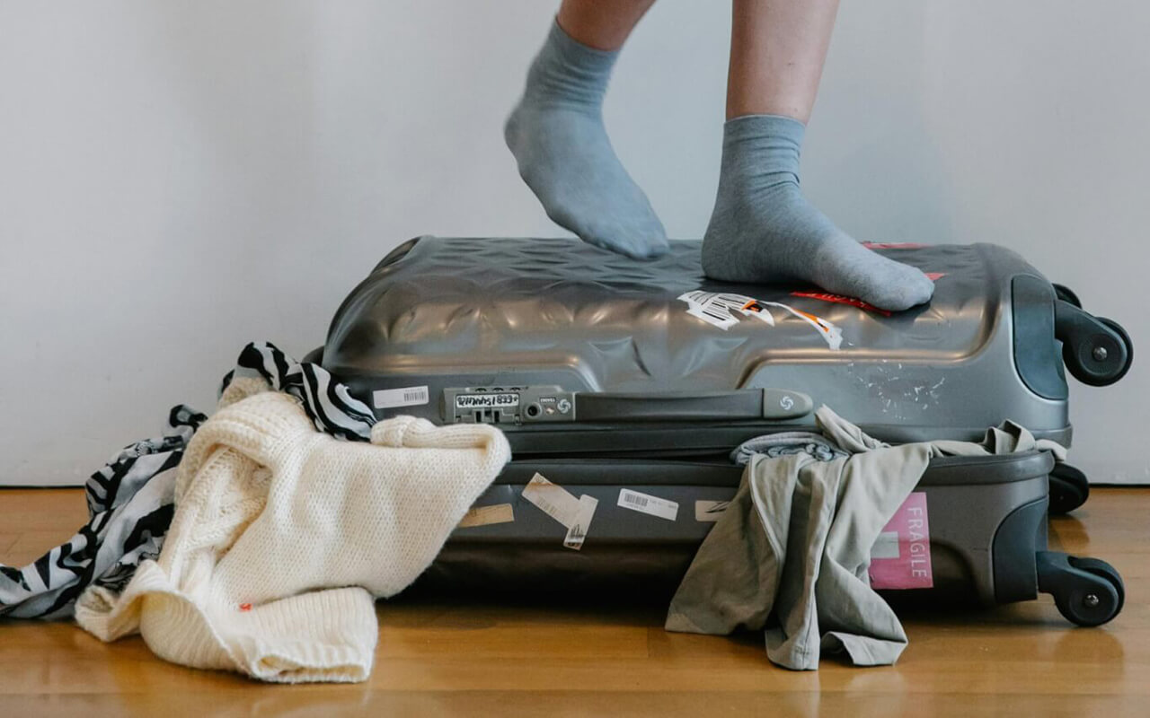 Person standing on a messy suitcase with grey socks.