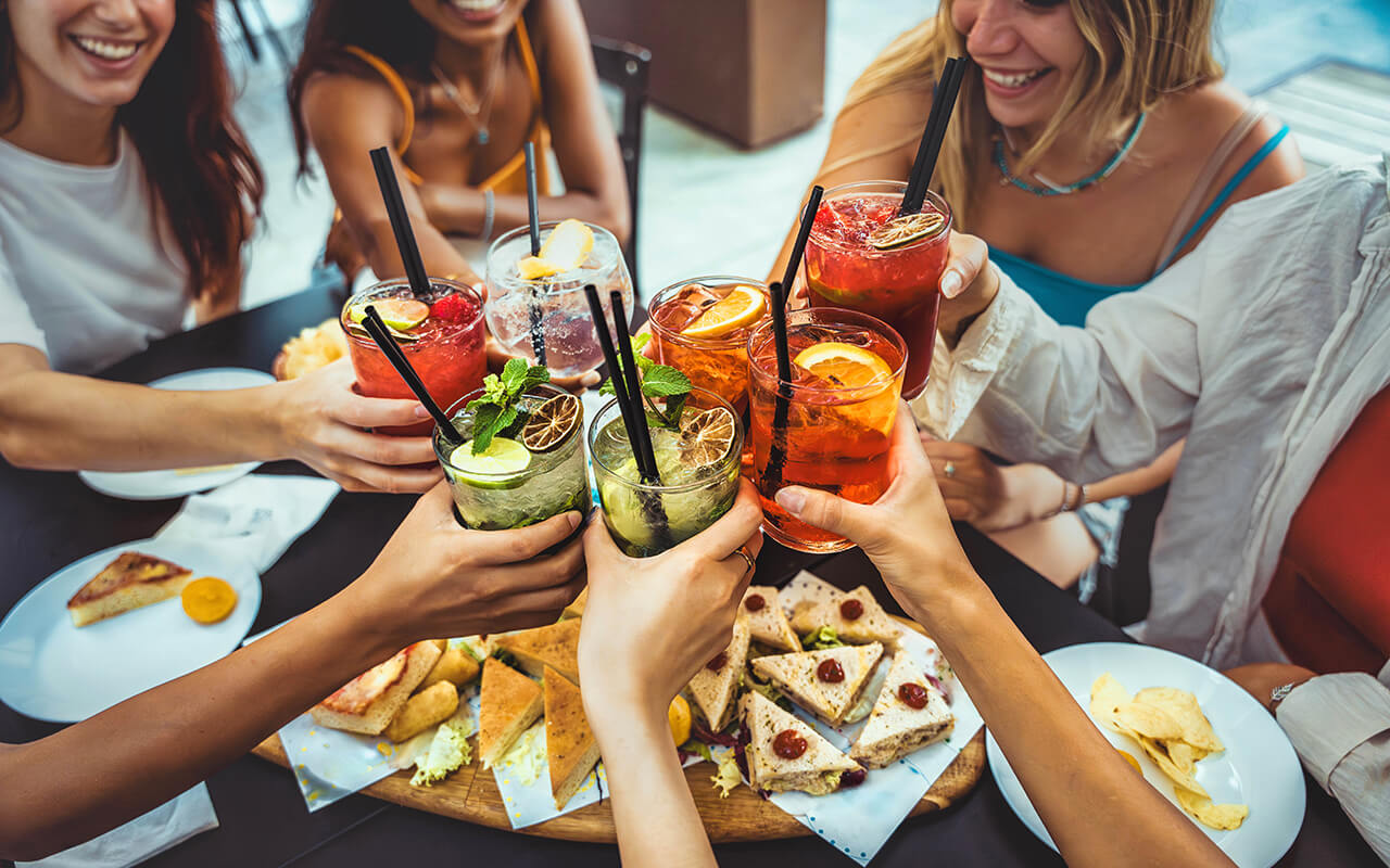 Happy female people toasting cocktail glasses sitting at bar table