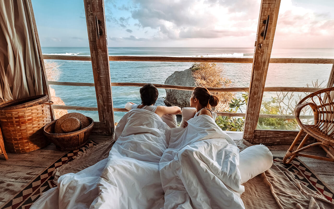Couple relaxing in bed at an oceanfront bungalow during sunrise