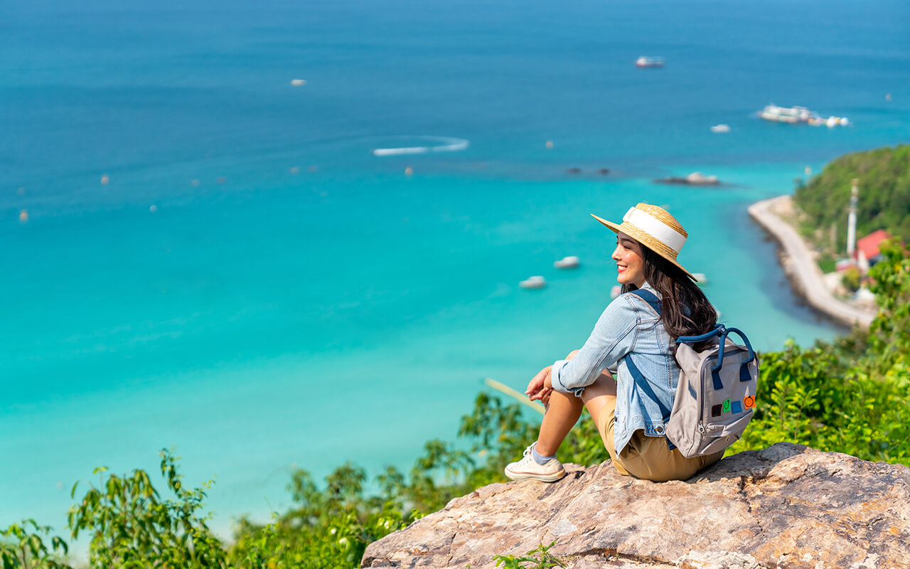 Solo traveler sitting on a cliff overlooking turquoise ocean water