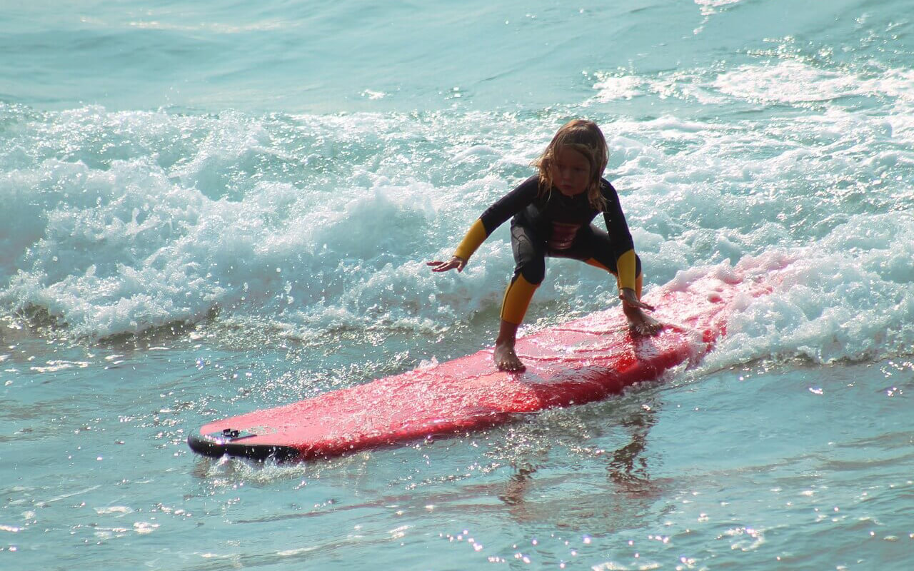 A young kid surfing on a red surfboard.
