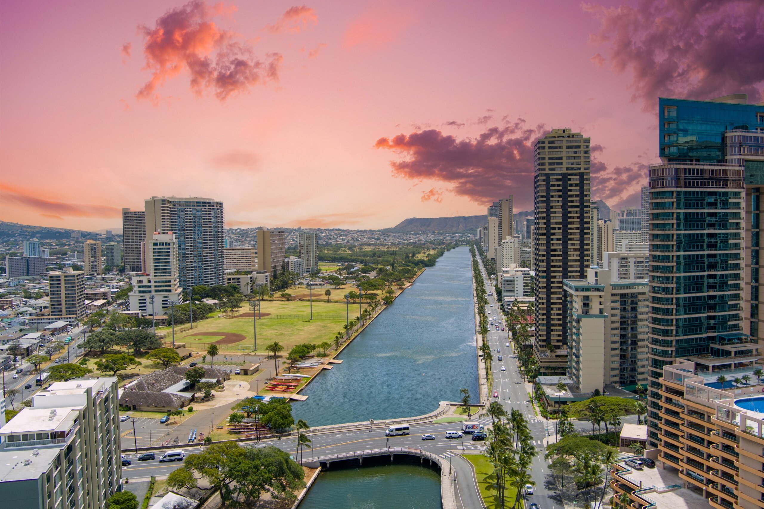 Ala Wai Canal with skyscrapers, hotels and condos, lush green trees, cars on the street and powerful clouds at sunset in downtown Honolulu Hawaii USA