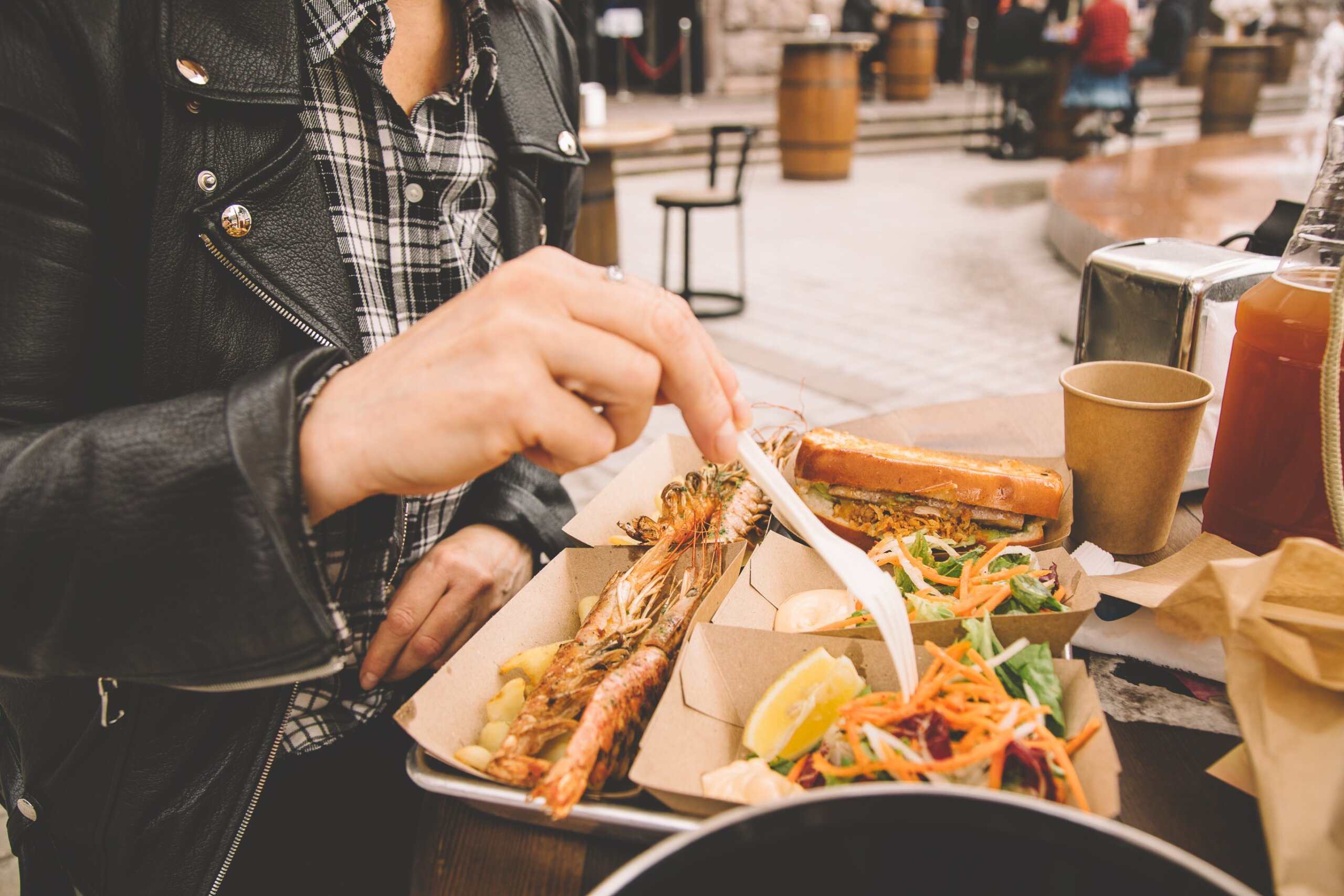 A woman's hand takes the ready-to-eat shrimp. Sea food in paper boxes on the table. Street food