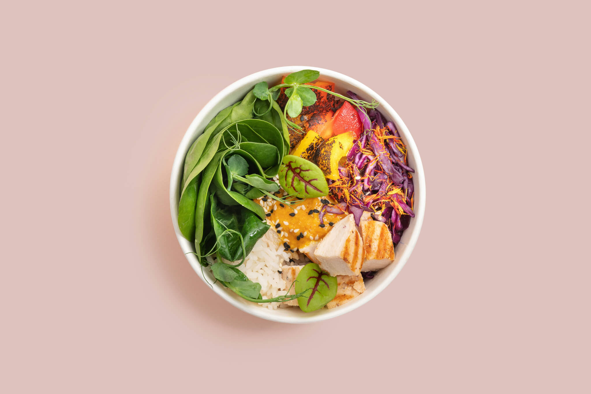 Salad with many ingredients in a bowl over a pink background