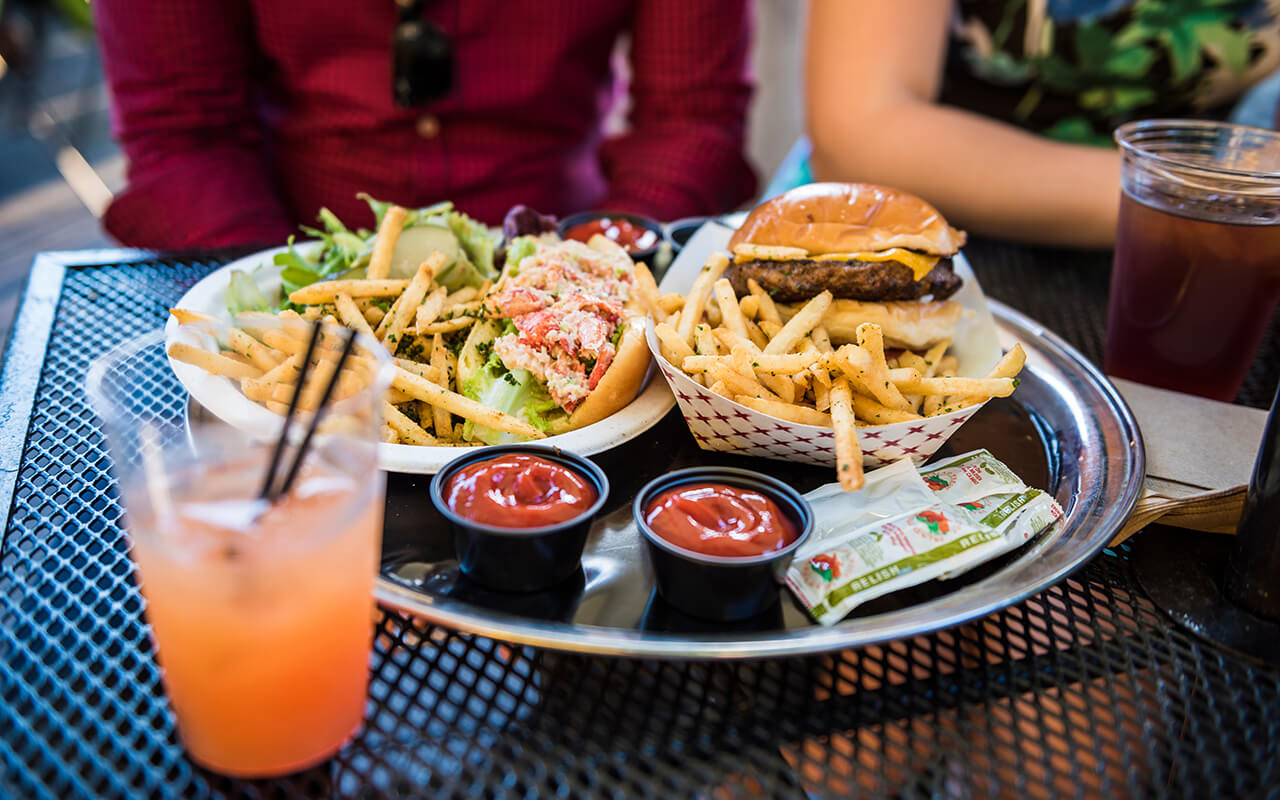 Food, lobster roll, salad, ketchup, relish and burger with fries, and drinks with two people sitting in New York City