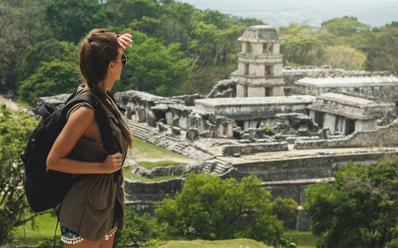 Woman with a backpack beside ancient Mayan ruins
