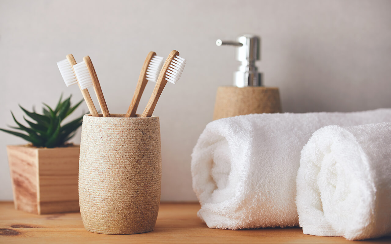 Four bamboo toothbrushes in a cup and white towels