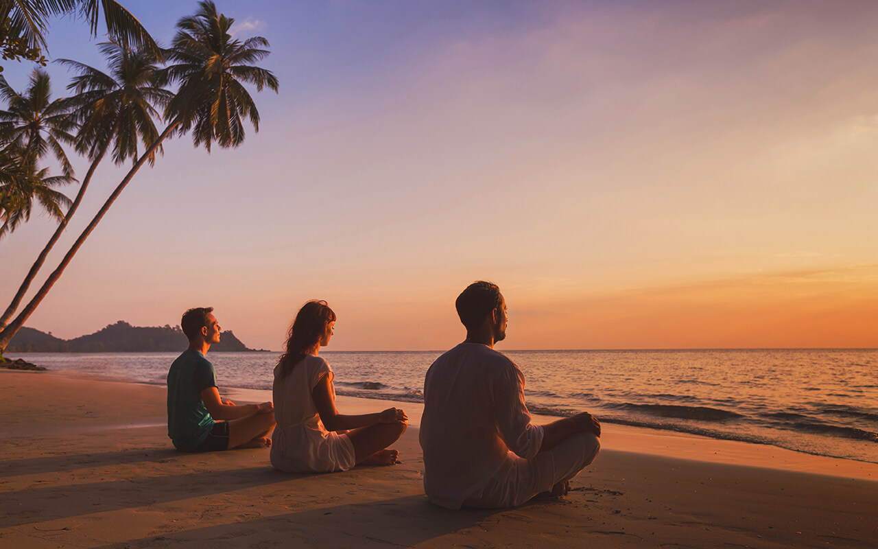 Three people doing yoga on the beach