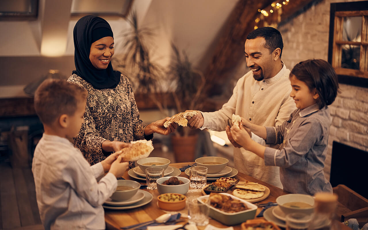 Happy Middle Eastern family shares pita bread at dining table on Ramadan.