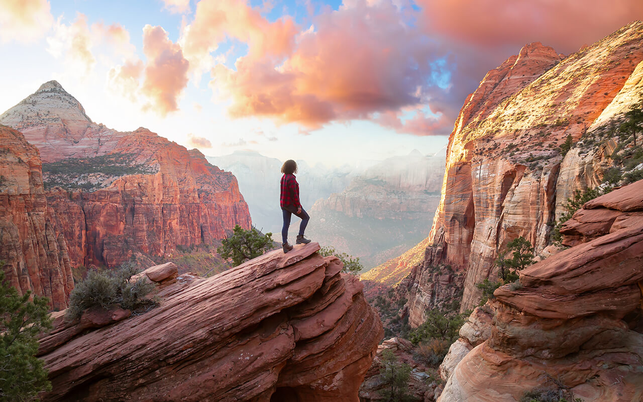 Adventurous Woman at the edge of a cliff is looking at a beautiful landscape view in the Canyon during a vibrant sunset. 