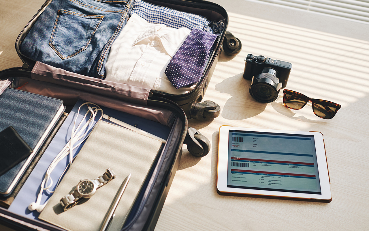 Packed suitcase with sunglasses, tablet, camera, watch and headphones 