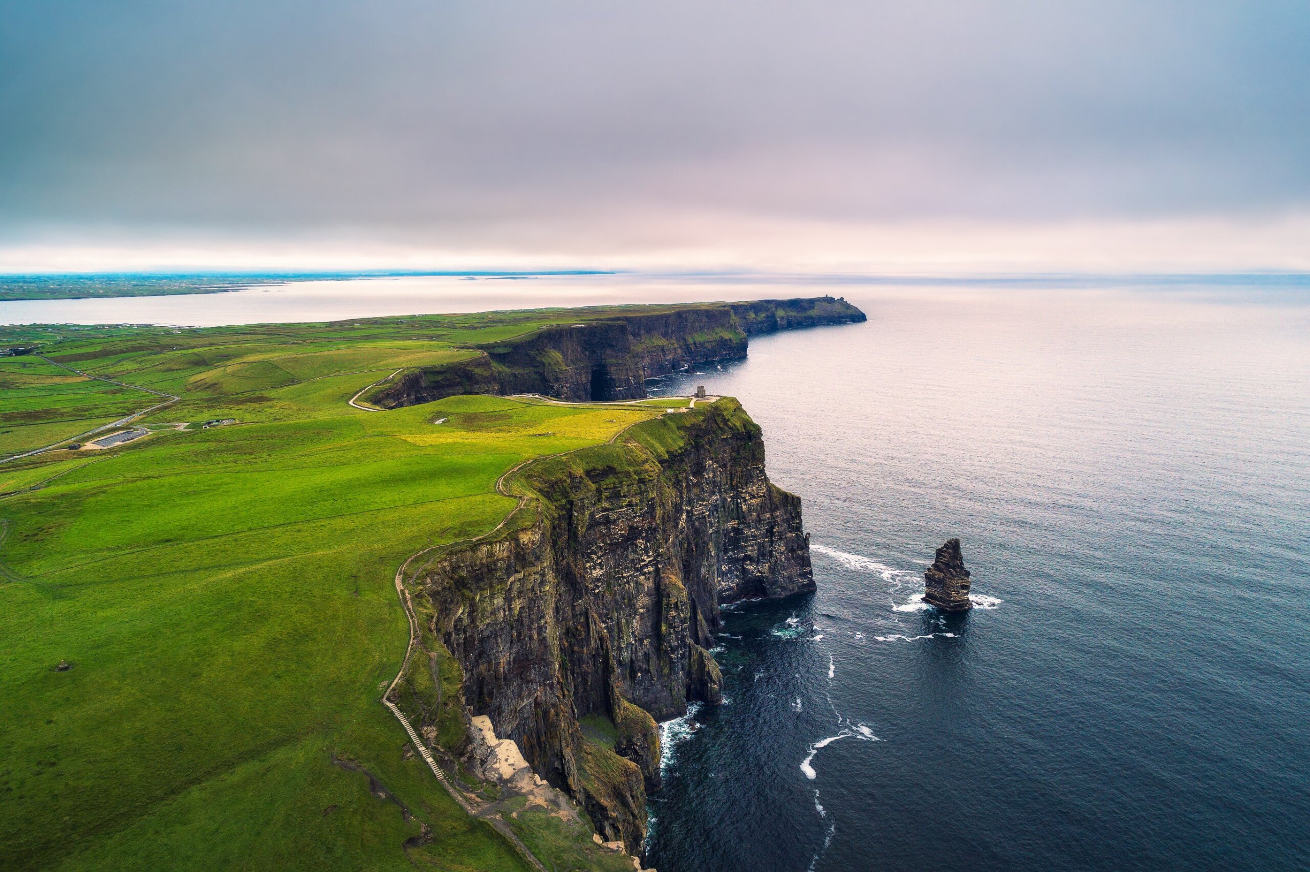 Aerial view of the Cliffs of Moher with green fields atop steep sea cliffs along the Atlantic coast in Ireland.